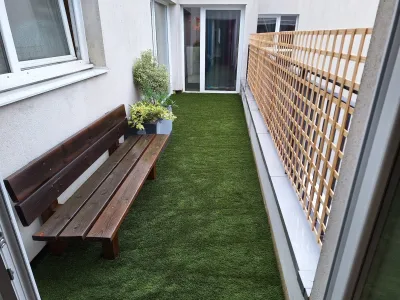 Couloir extérieur avec banc en bois, pelouse synthétique et treillage brise-vue