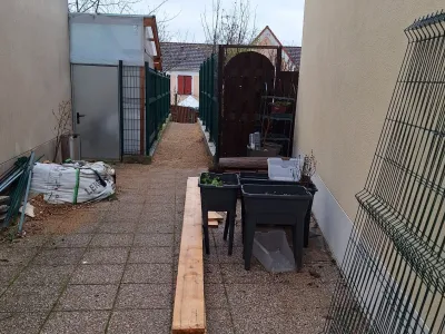 Cour arrière avec pavés, jardinières et outils de jardinage disposés, accès à un portail en bois.