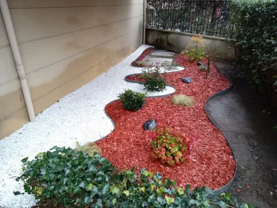 Jardin avec gravier blanc et paillis rouge, allée courbe et végétation.