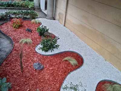 Jardin avec gravier blanc et paillis rouge, plantes en massifs décoratifs.