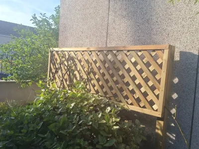 Treillis bois installé contre un mur avec plantes grimpantes autour.