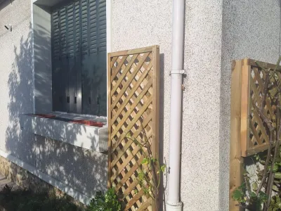 Treillis bois installé contre un mur avec ombre sur la façade.