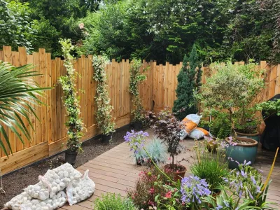 Clôture en bois avec plantations décoratives et terrasse en bois dans un jardin paysager