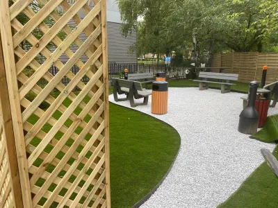 Aménagement finalisé avec allée blanche, bancs, poubelles et pelouse artificielle