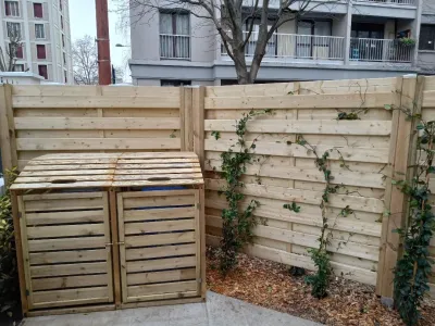 Deux composteurs en bois contre une clôture en panneaux de bois avec plante grimpante