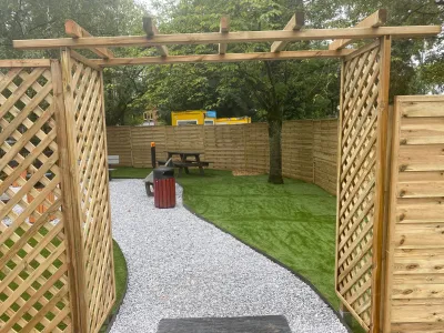 Entrée de jardin avec treillage en bois, allée en gravier et pelouse synthétique