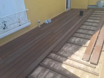 Pose de terrasse en bois en cours sur support préparé contre une façade