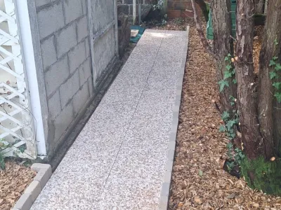 Allée piétonne pavée et bordée de paillis marron, entourée de murs et plantes.