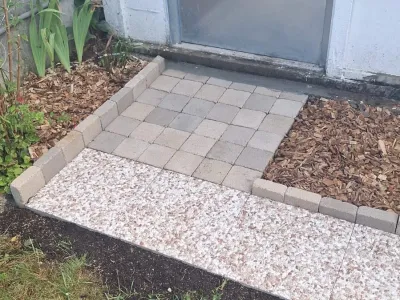 Petite aire pavée carrée avec bordures en béton et paillis, devant un mur