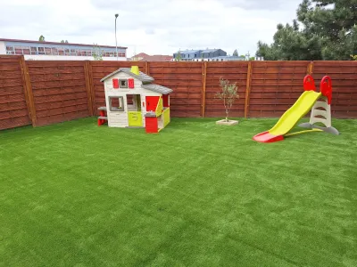 Aire de jeux pour enfants avec pelouse synthétique, toboggan et maisonnette dans un jardin clos