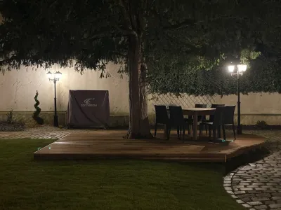 Terrasse en bois avec table et chaises sous un arbre, éclairage de jardin nocturne