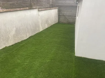 Pelouse synthétique posée le long d’un mur pour un aménagement extérieur propre et durable