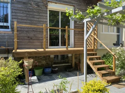 Terrasse en bois surélevée avec garde-corps et végétation autour.