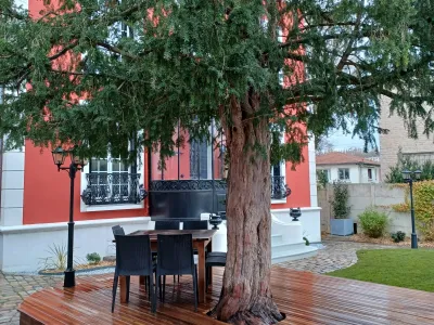 Terrasse en bois aménagée devant maison rouge avec table, chaises et grand arbre