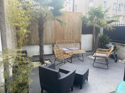 Terrasse avec fauteuils noirs et table, plantes et palissade en arrière-plan.