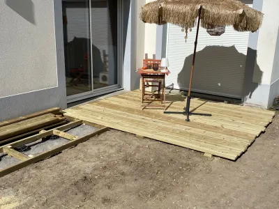 Terrasse bois presque terminée avec parasol et mobilier, bordure mur blanc.