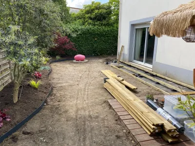 Jardin en préparation avec sol nu et planches de bois alignées le long de la maison.
