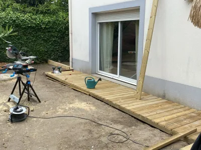 Jardin en préparation avec sol nu et planches de bois alignées le long de la maison.