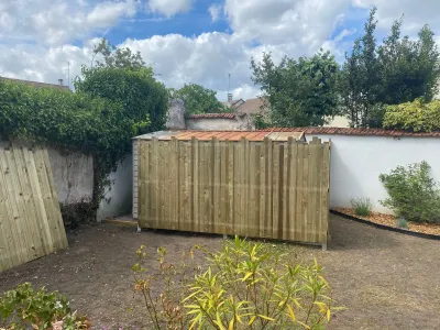 Vue d’ensemble de l’abri de jardin entouré d’une nouvelle clôture en bois, jardin non aménagé autour.