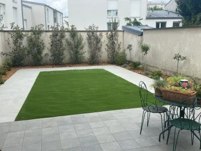Jardin urbain aménagé avec pelouse synthétique encadrée par une terrasse en dalles