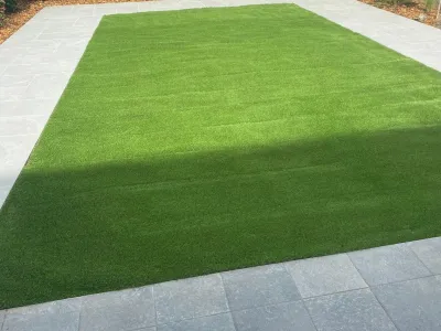 Pelouse synthétique posée au centre d’une terrasse minérale dans un espace extérieur privé