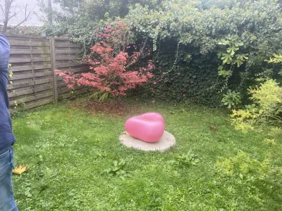 Petit jardin avec arbre et sculpture rose, clôture bois en arrière-plan.