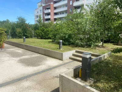 Petit espace vert avec allée pavée et arbres, entouré de murs bas