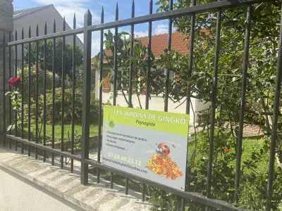 Clôture métallique avec panneau de signalisation d’entreprise de paysagisme et jardin derrière