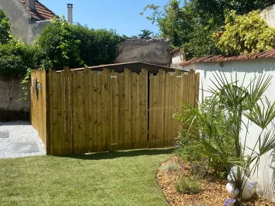 Clôture en bois courbe intégrée dans un jardin avec pelouse et végétation exotique