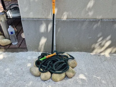 Tuyau d’arrosage enroulé sur un tas de pierres dans un coin de jardin