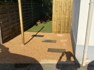 Allée en gravier clair menant vers un coin de jardin avec clôture en bois