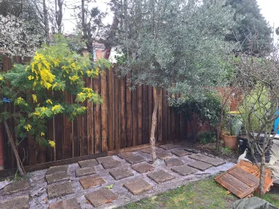Jardin avec arbres et palissade en bois, zone dallée partiellement installée